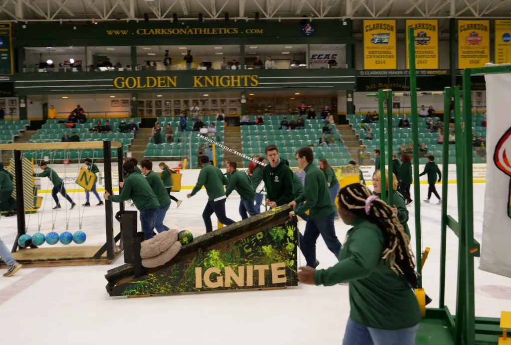 A group of students move pieces of a large Rube Goldberg machine on the ice of Cheel Arena.