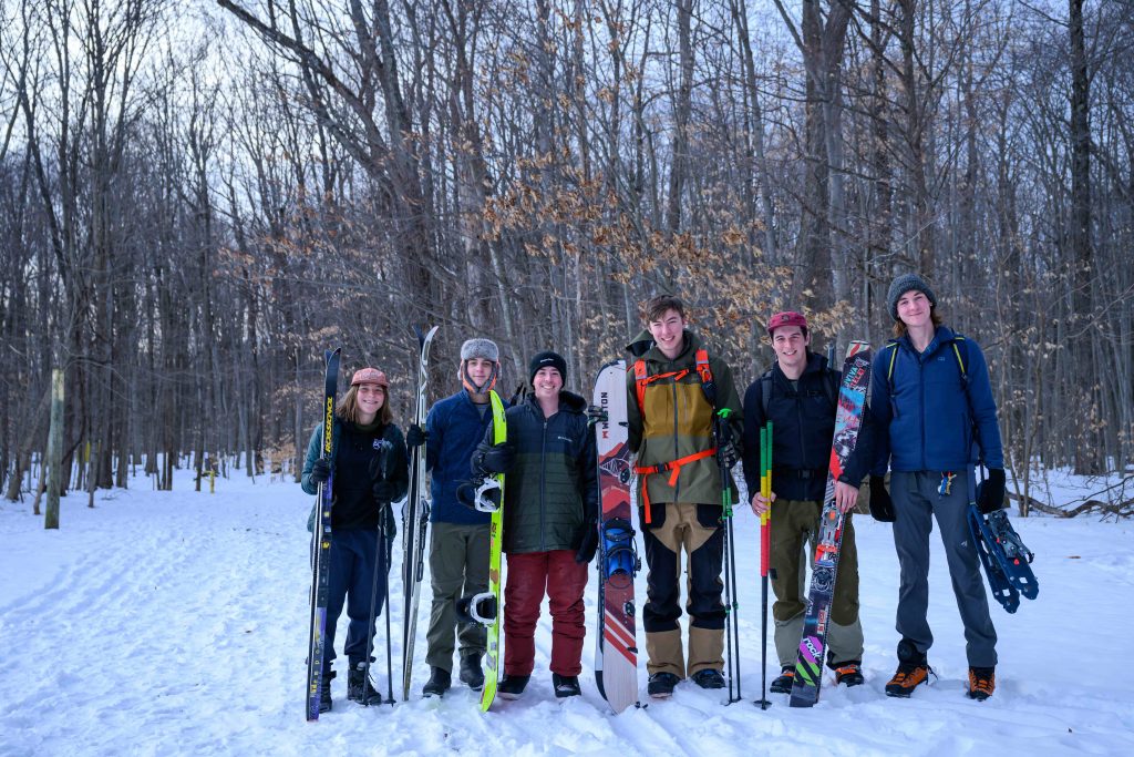 A group of Clarkson University students stand in a snowy landscape with ski equipment and gear.