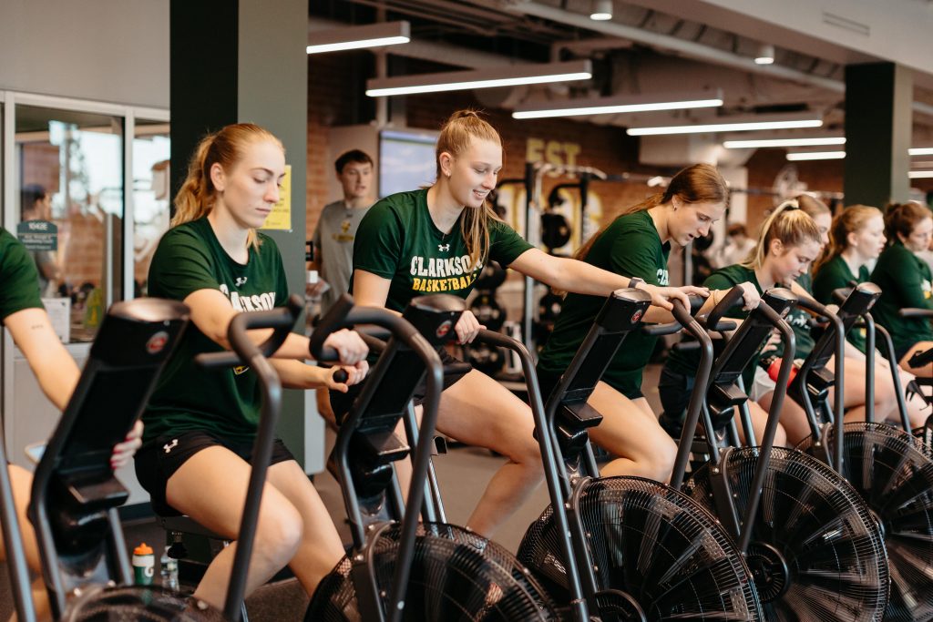 A group of female student athletes exercise on bikes in a gym at Clarkson University 