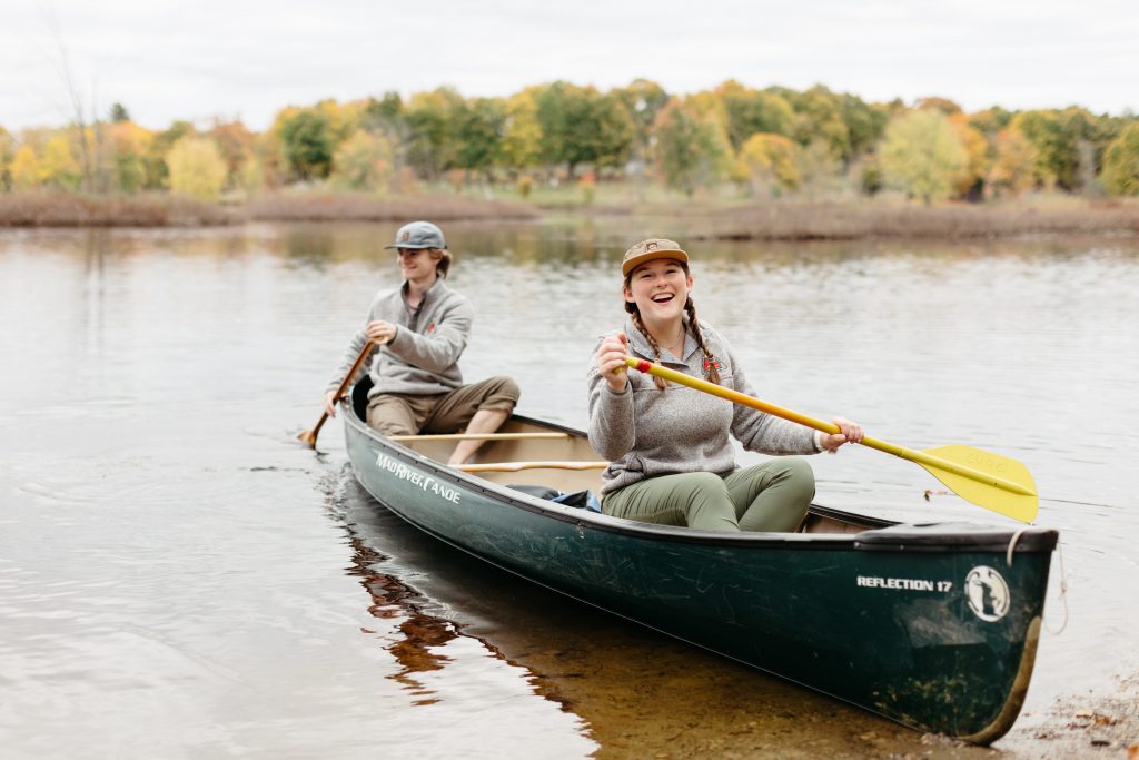 A male and female student sit in a canoe on the Raquette River