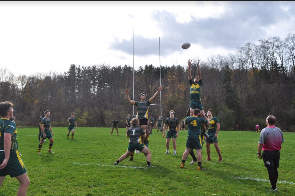 A group of male students on a field play rugby a Clarkson University