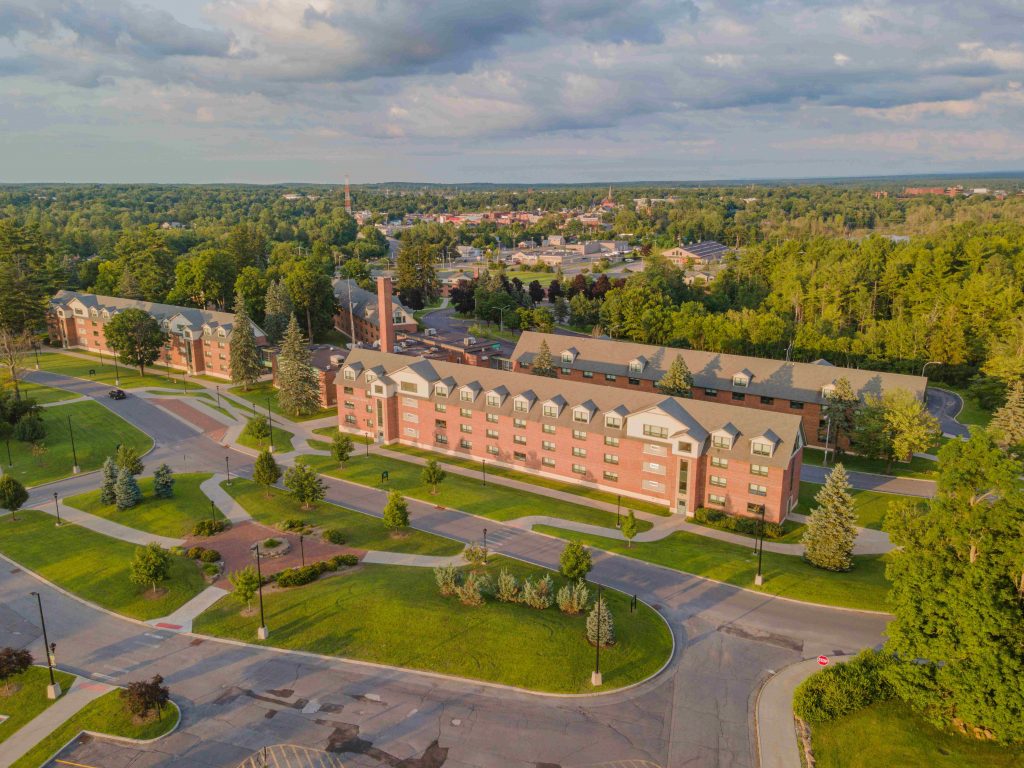 Aerial view of Clarkson University’s first-year residential quad on a sunny day, surrounded by greenery and showcasing the campus’s traditional brick dorm buildings.