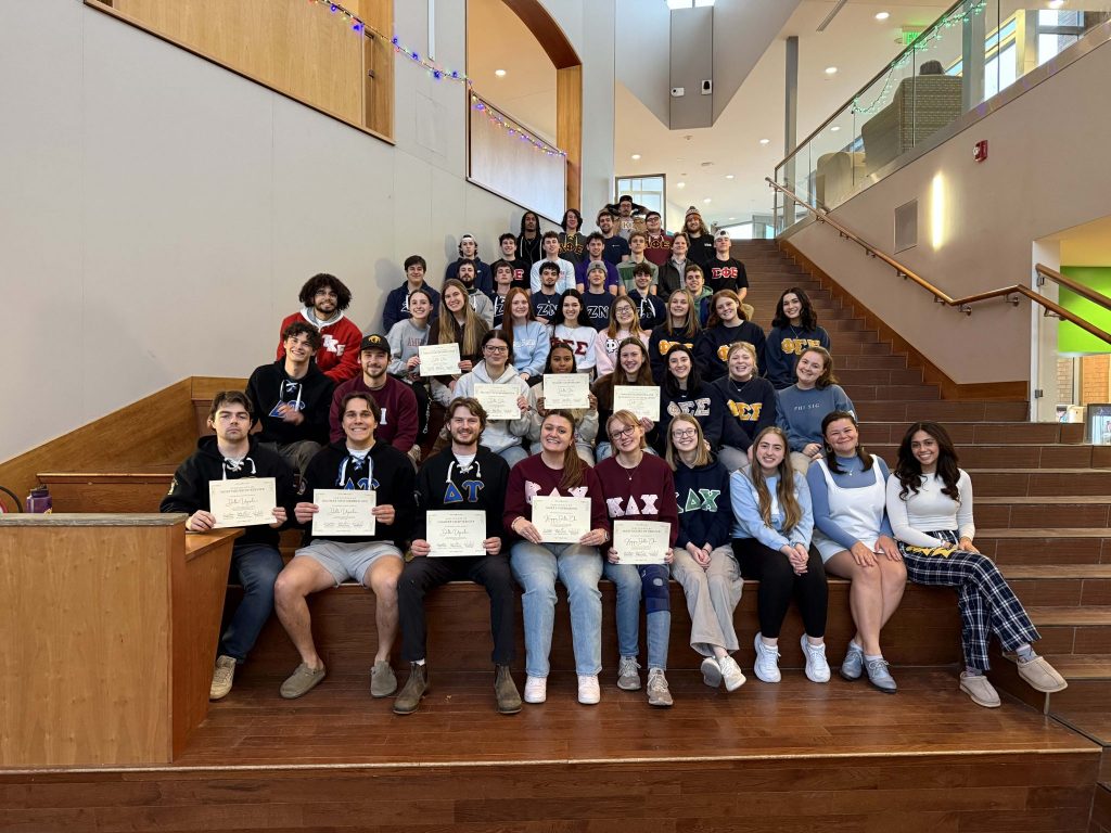 Group of Clarkson fraternity and sorority members seated on campus stairs, proudly holding achievement certificates.