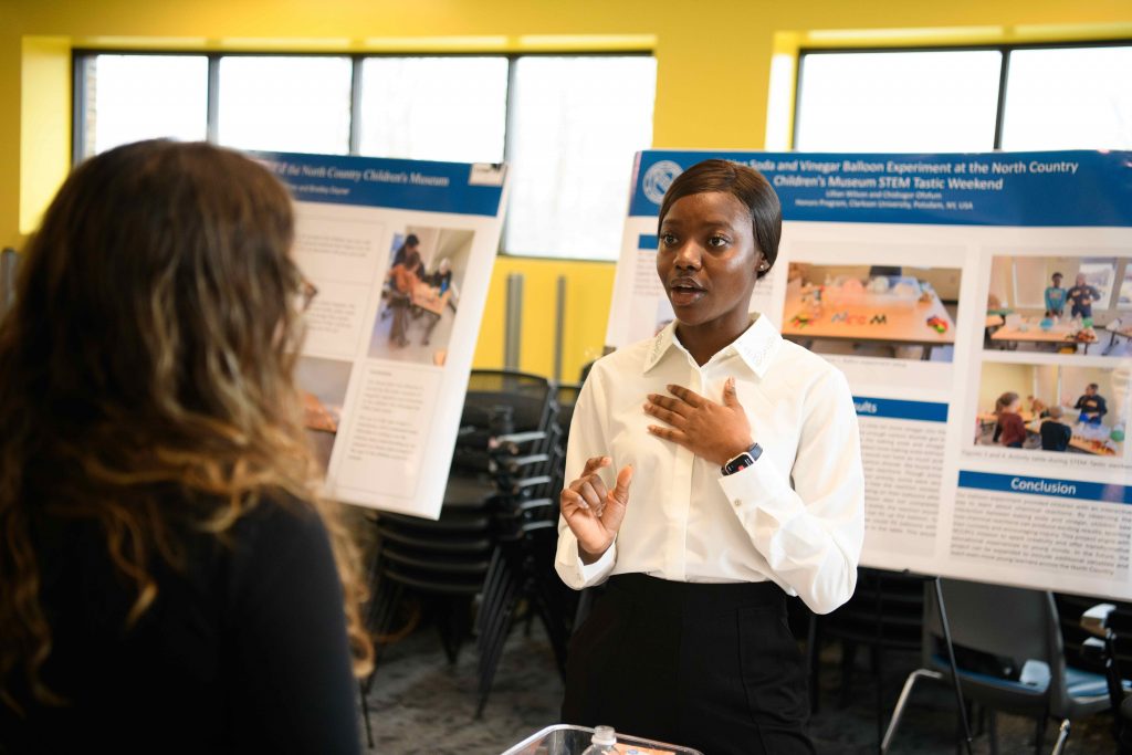 Student presents a STEM outreach project during Clarkson’s Ignite Expo, speaking in front of her research poster.