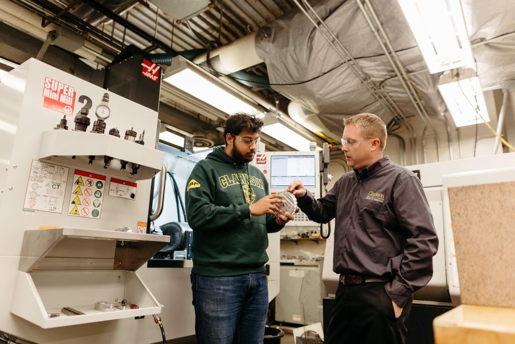 A Clarkson student receives guidance from a machine shop supervisor while examining a prototype part.
