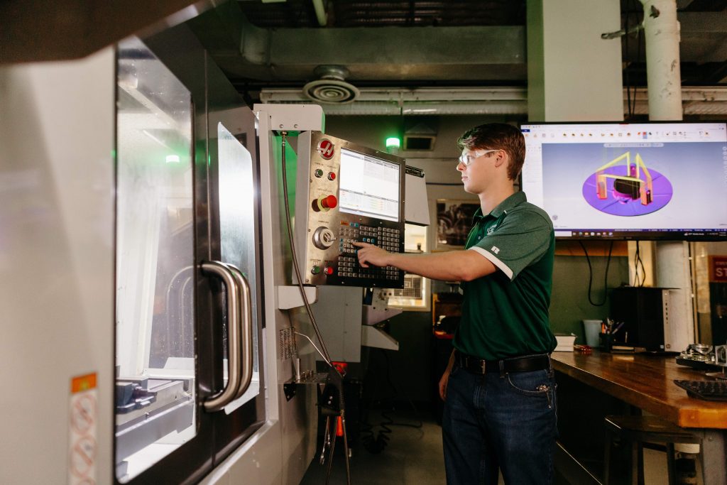 A Clarkson student operates a CNC mill while referencing a CAD model in the SPEED lab.