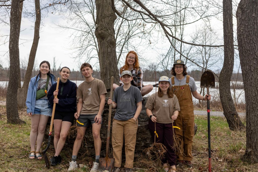 Group of Clarkson students with shovels pose in a wooded area after a community tree planting project.
