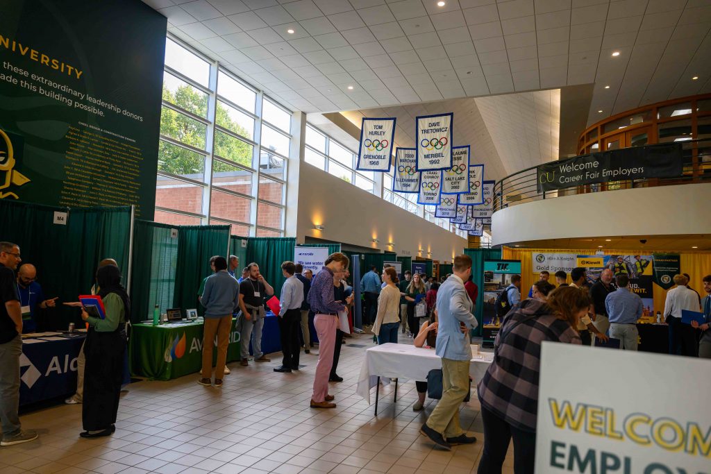 Students and employers networking at Clarkson University’s Fall Career Fair in the Student Center, with company booths and banners displayed.