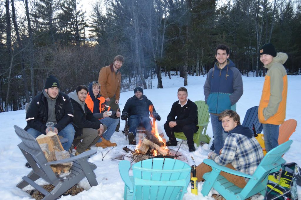 Members of Clarkson’s SPEED team gather around a fire pit in the snow, smiling and enjoying team bonding time outdoors.