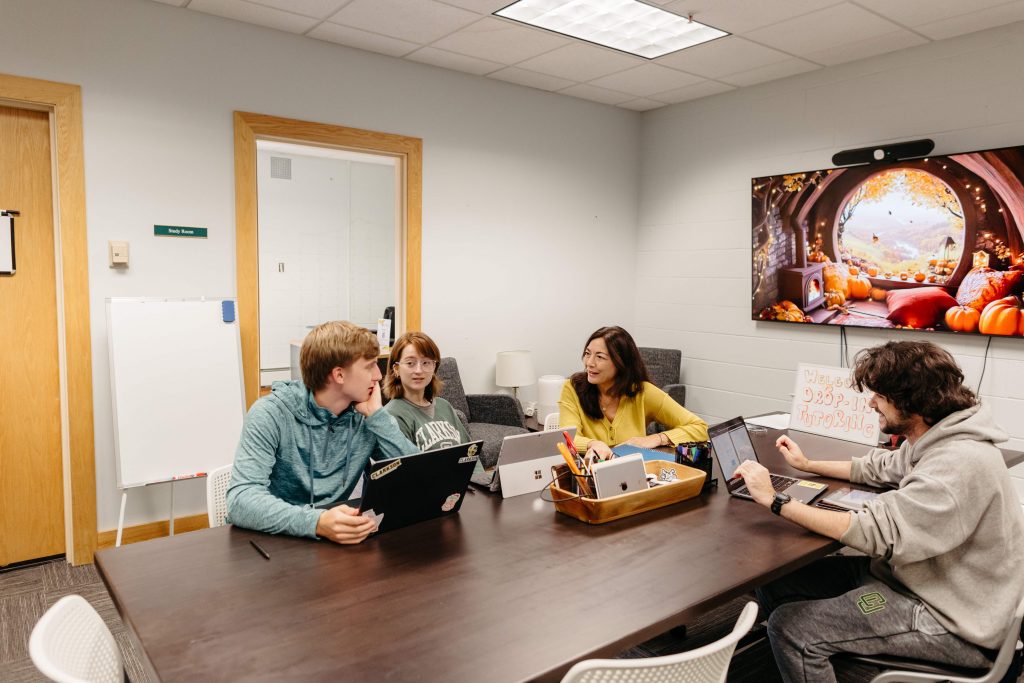 Students working with a tutor during a drop-in tutoring session at Clarkson University, seated around a study table with laptops.