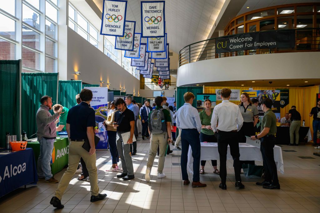 Students engaging with company representatives at various booths inside Clarkson’s Cheel Center during the 2025 Fall Career Fair. Olympic banners hang overhead and natural light fills the space.