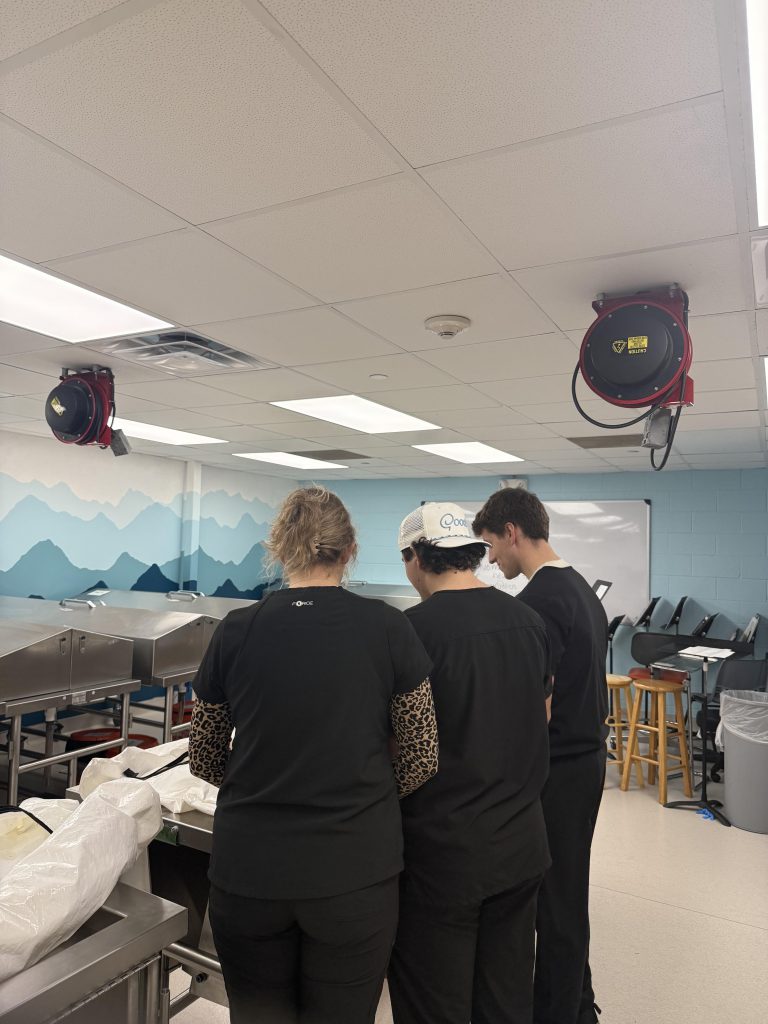 Three clarkson Students standing facing away from the camera looking at an object.