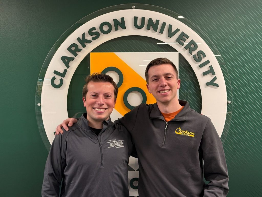 A picture of Miles and Owen Compani in front of a Clarkson logo