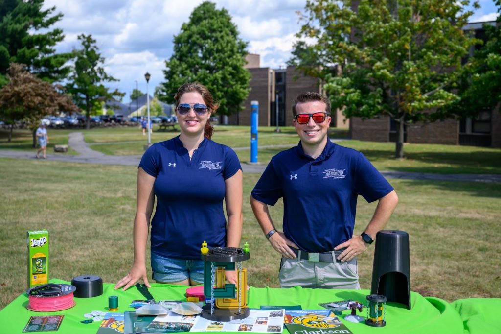 Two students stand in front of a table displaying various Clarkson Ignite items.