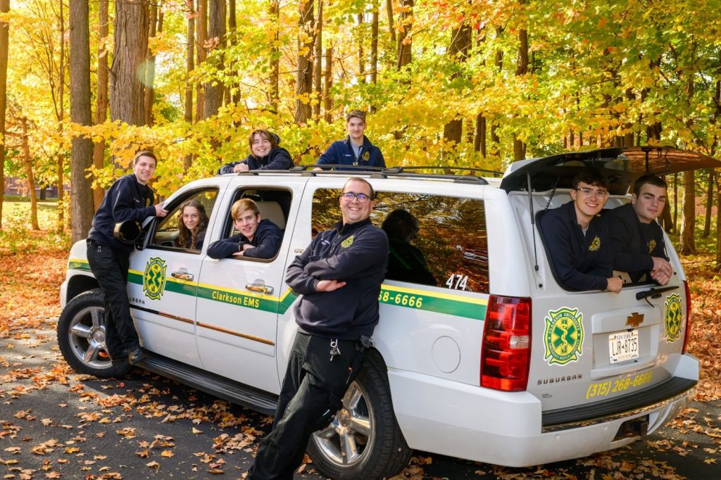 A group of students, wearing CUEMS gear, stand around a customized suburban vehicle.
