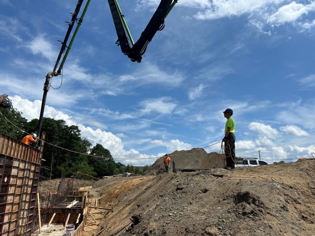 A male student stands on a mound of dirt at a construction site, with heavy equipment nearby.
