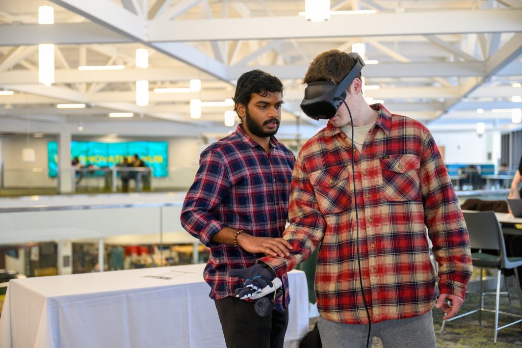 A Clarkson student wearing a virtual reality headset and controller participates in a VR demonstration while another student stands beside them offering assistance in the ERC.