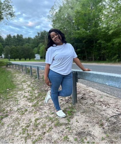 This is an image of a young college student who is smiling for the camera while participating in a solo hike alongside a roadway.