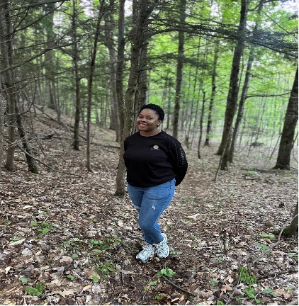 This is an image of a young college student standing in the woods. She is smiling for the camera.