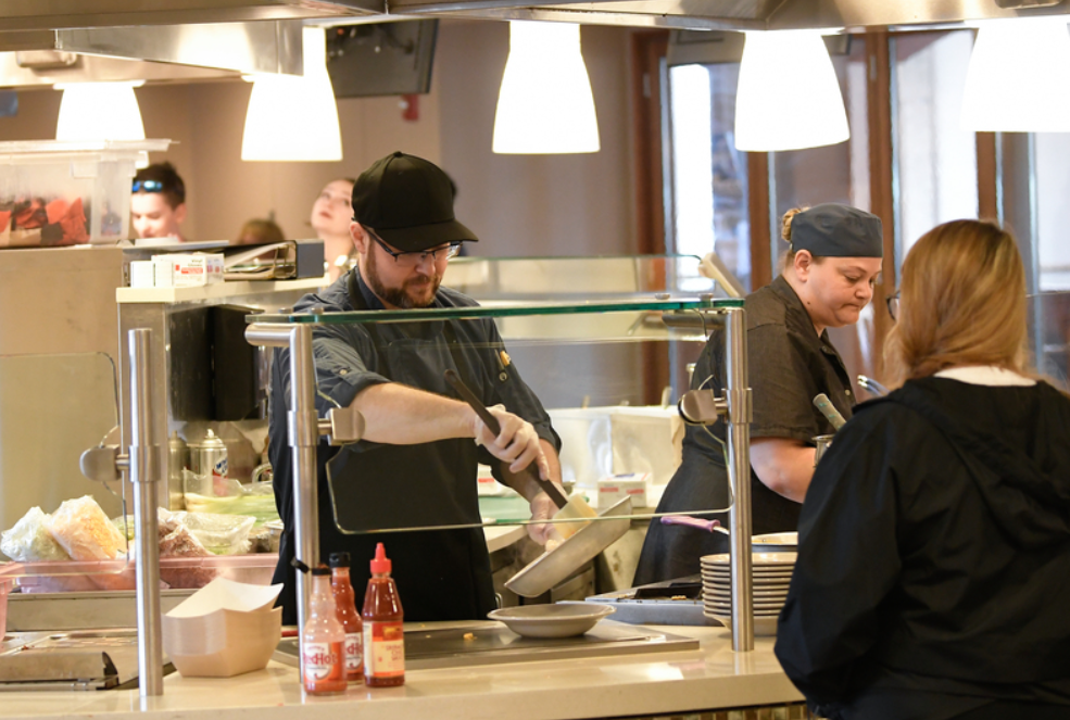 Two workers at student center servery, serving food to students.