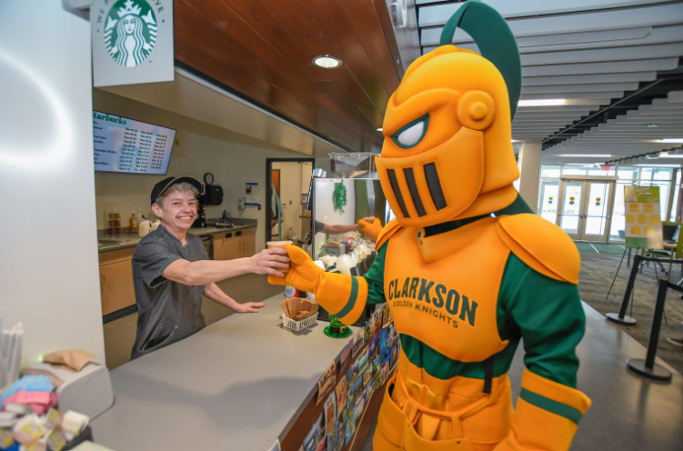 Worker at Schuler's Cafe serving a coffee to the Clarkson University golden knight mascot. 